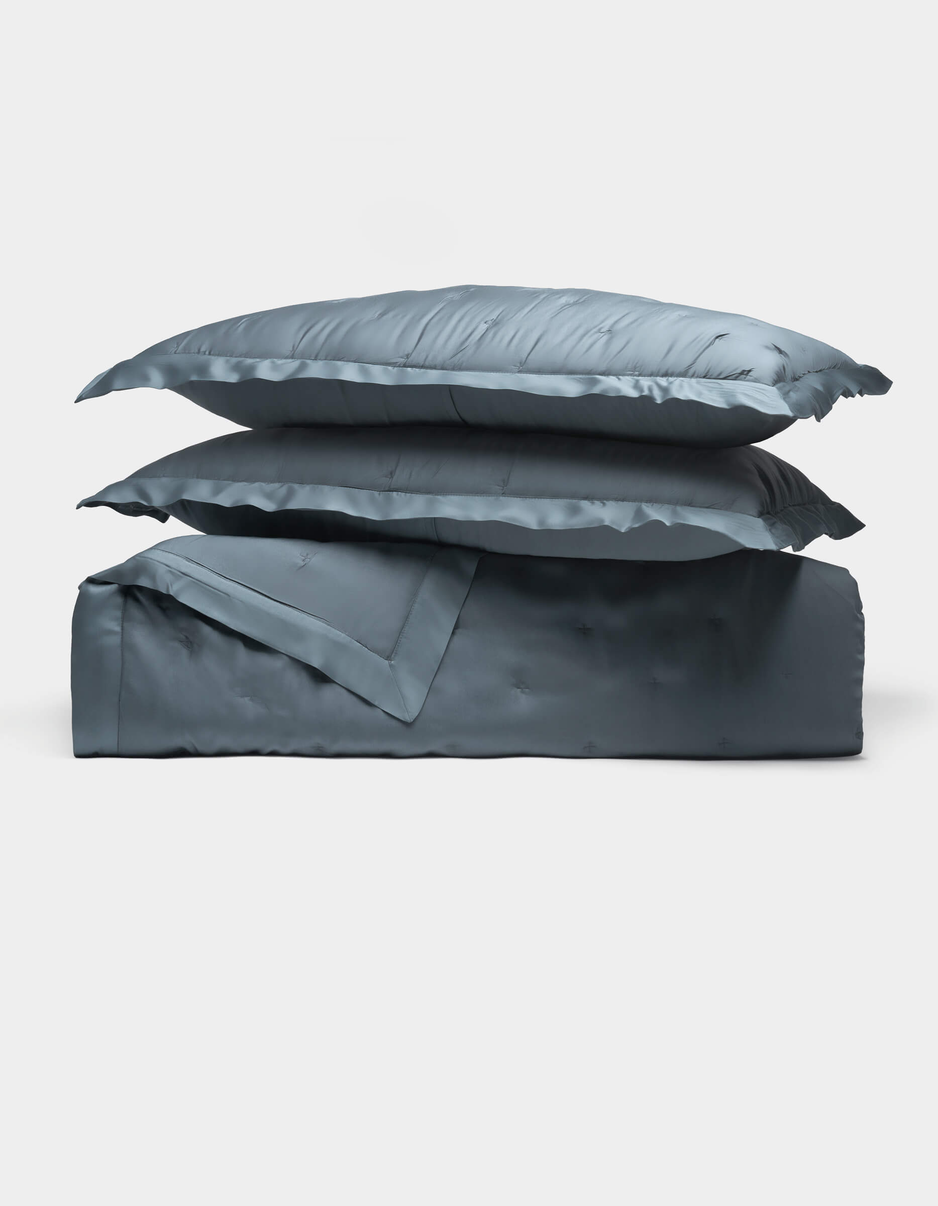 Two Cozy Earth Bamboo Quilt Bundle blue satin pillows are stacked atop a matching folded comforter, all set against a plain white background.|Color:Pacific Blue