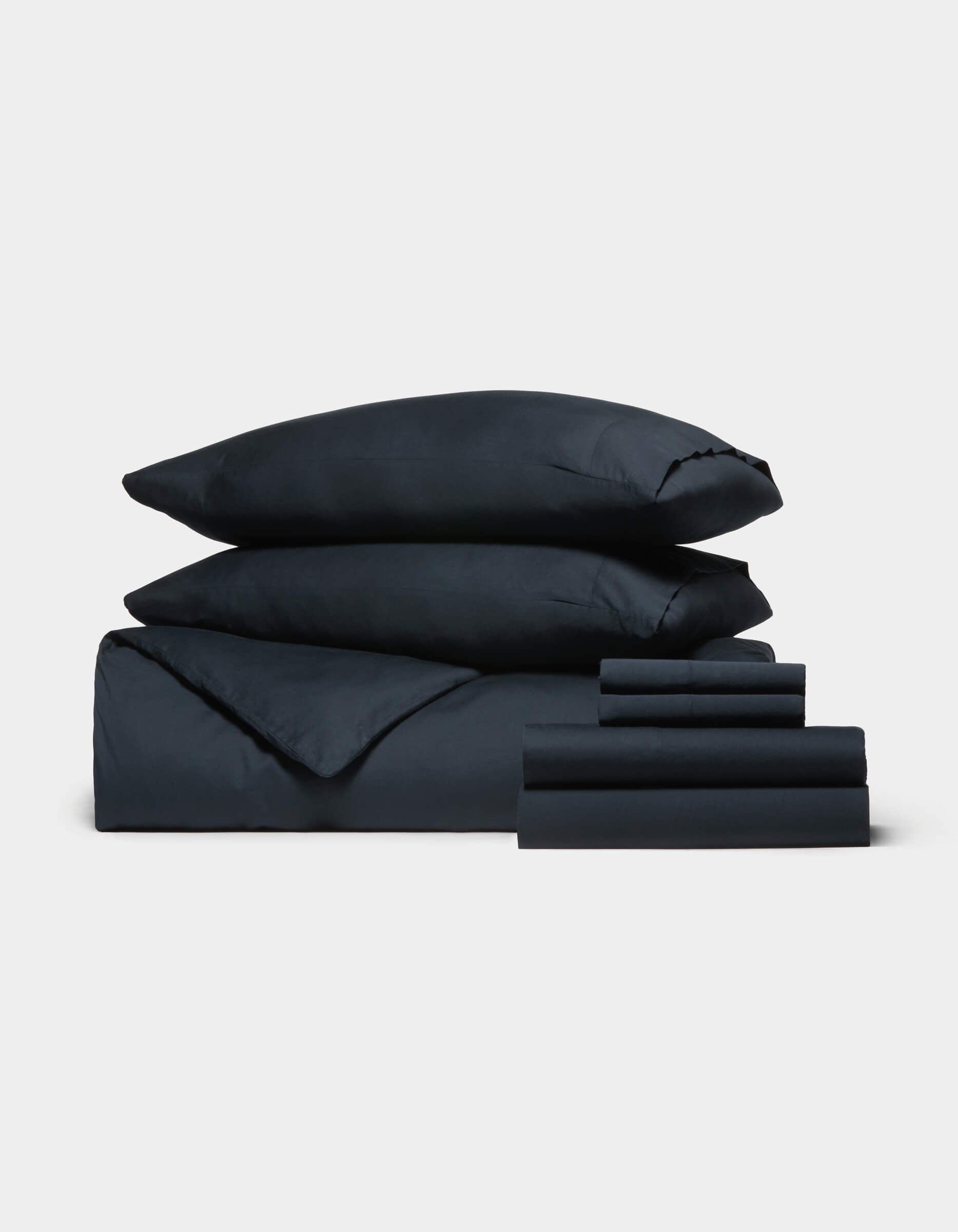 The Cozy Earth Soft-Wash Cotton Bedding Core Bundle, featuring two stacked pillows, a duvet, and several sheets in dark navy blue, is neatly arranged against a plain white background.|Color:Eclipse