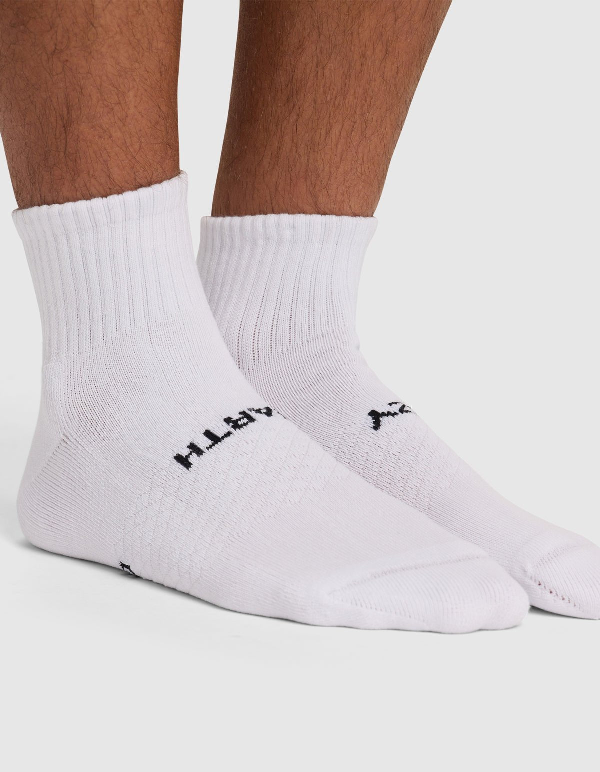 A person wears Cozy Earth's Essential Quarter Sock, a white ribbed crew sock with "Happy" in black text near the arch, covering the ankles and part of the lower leg.|Color:Cedar