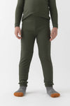 A child wears Cozy Earth’s Children’s Bamboo Waffle Knit Base Layer Pant in Olive, paired with a matching long-sleeve top and gray socks with orange toes, standing against a plain white background. The child’s face is not shown.|Color:Olive