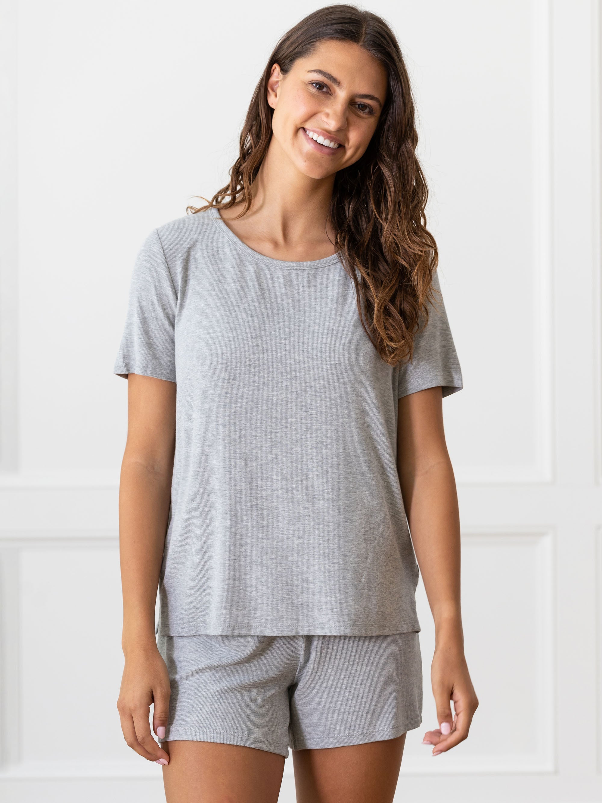 Woman wearing a grey Cozy Earth Rib Knit Short Sleeve Lounge Top and gray shorts against a white background 