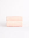 Two Luxe Hand Towels by Cozy Earth, in a soft pink hue, neatly folded and stacked against a white background. |Color:Blossom