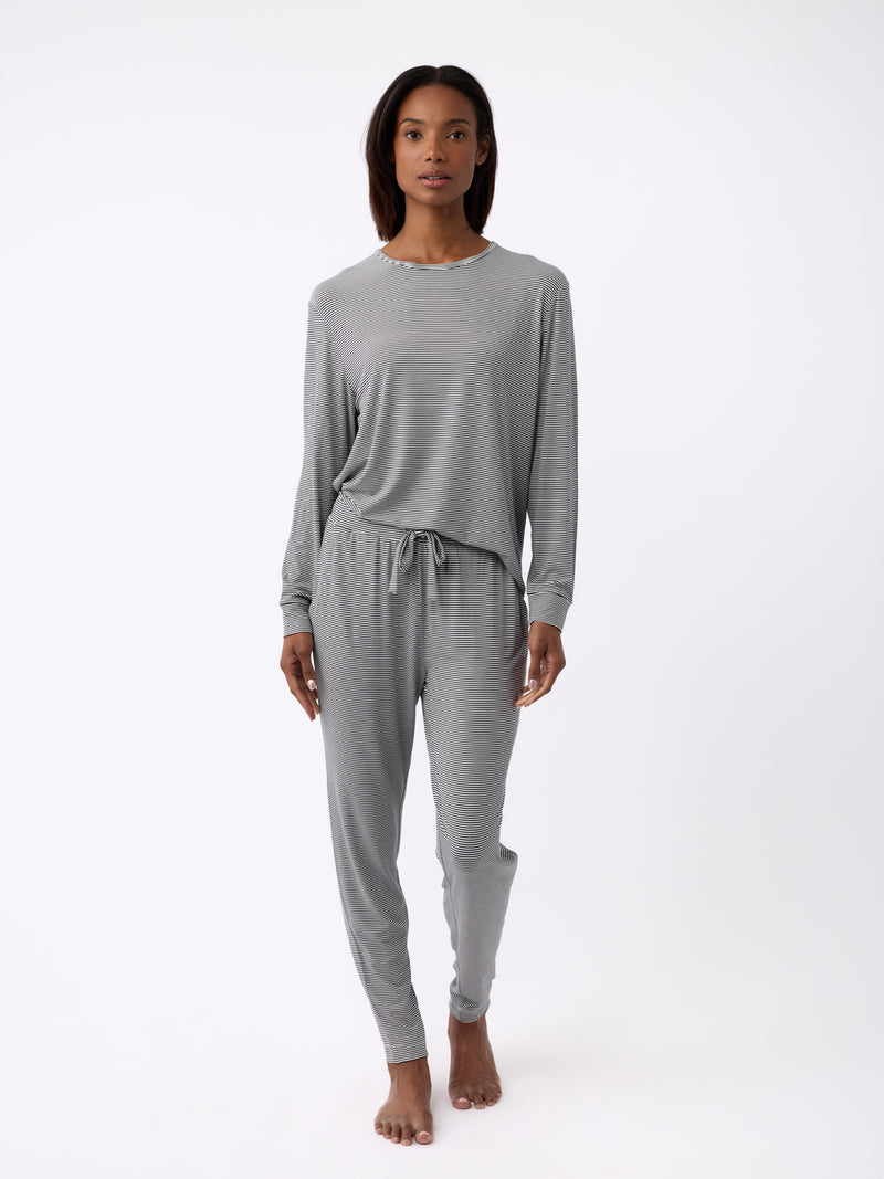 Against a white backdrop, a person barefoot sports the Cozy Earth set, featuring the Women's Bamboo Stretch-Knit Tapered Pant in grey. The outfit exudes comfort and relaxation.