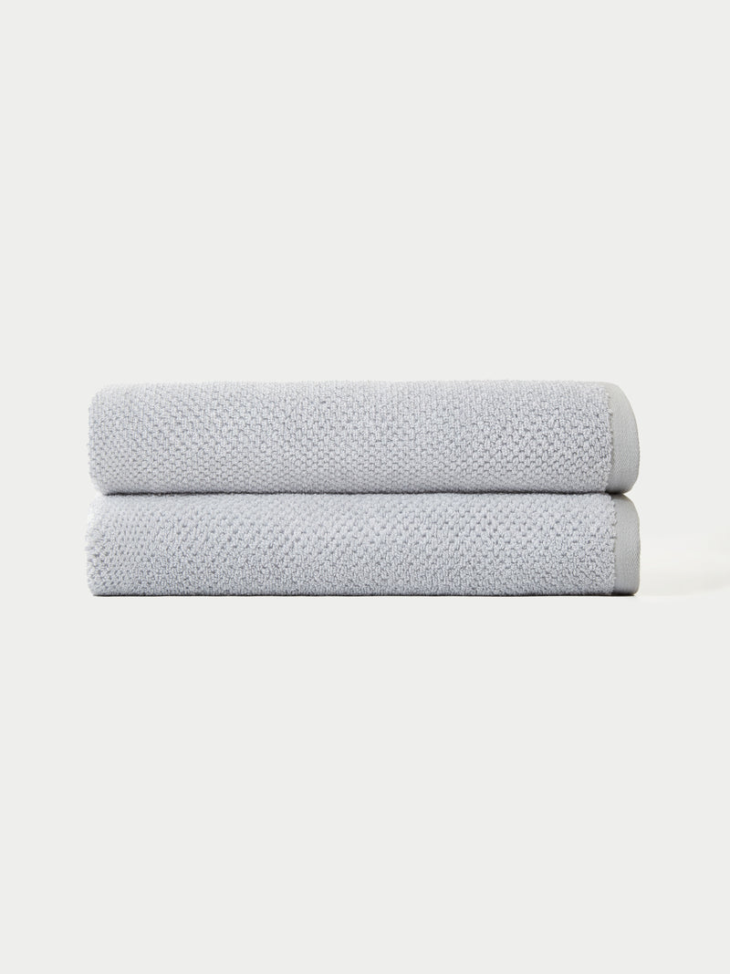 The Complete Nantucket Bath Bundle by Cozy Earth features two neatly folded light gray towels stacked on top of each other against a plain white background.