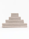 The Complete Nantucket Bath Bundle by Cozy Earth, featuring beige textured towels in various sizes, is neatly stacked pyramid-style on a white background.|Color:Heathered Sand