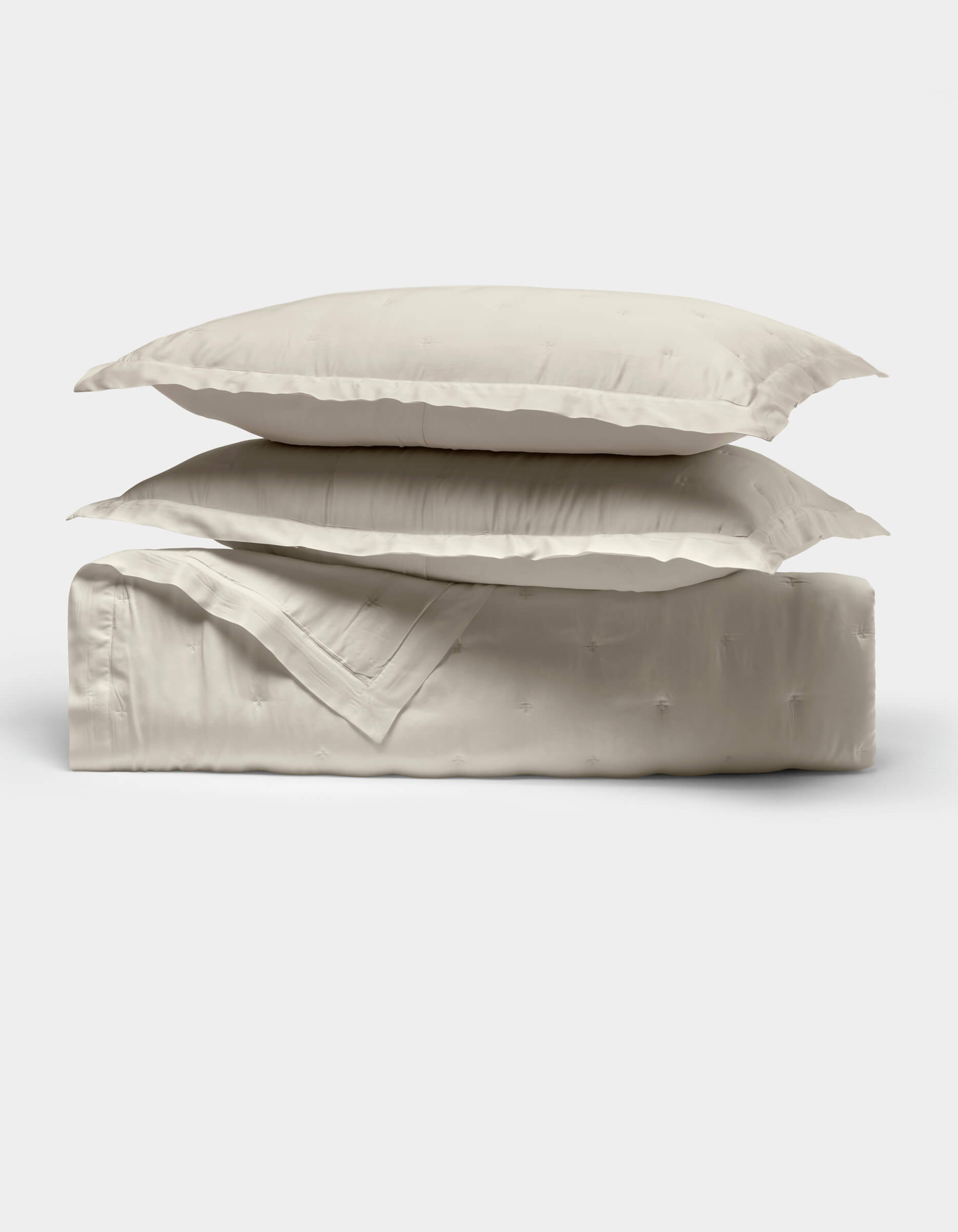 Two cream-colored pillows from Cozy Earth's Bamboo Quilt Bundle are stacked atop a neatly folded matching quilt, all displayed against a plain white background.|Color:Oat