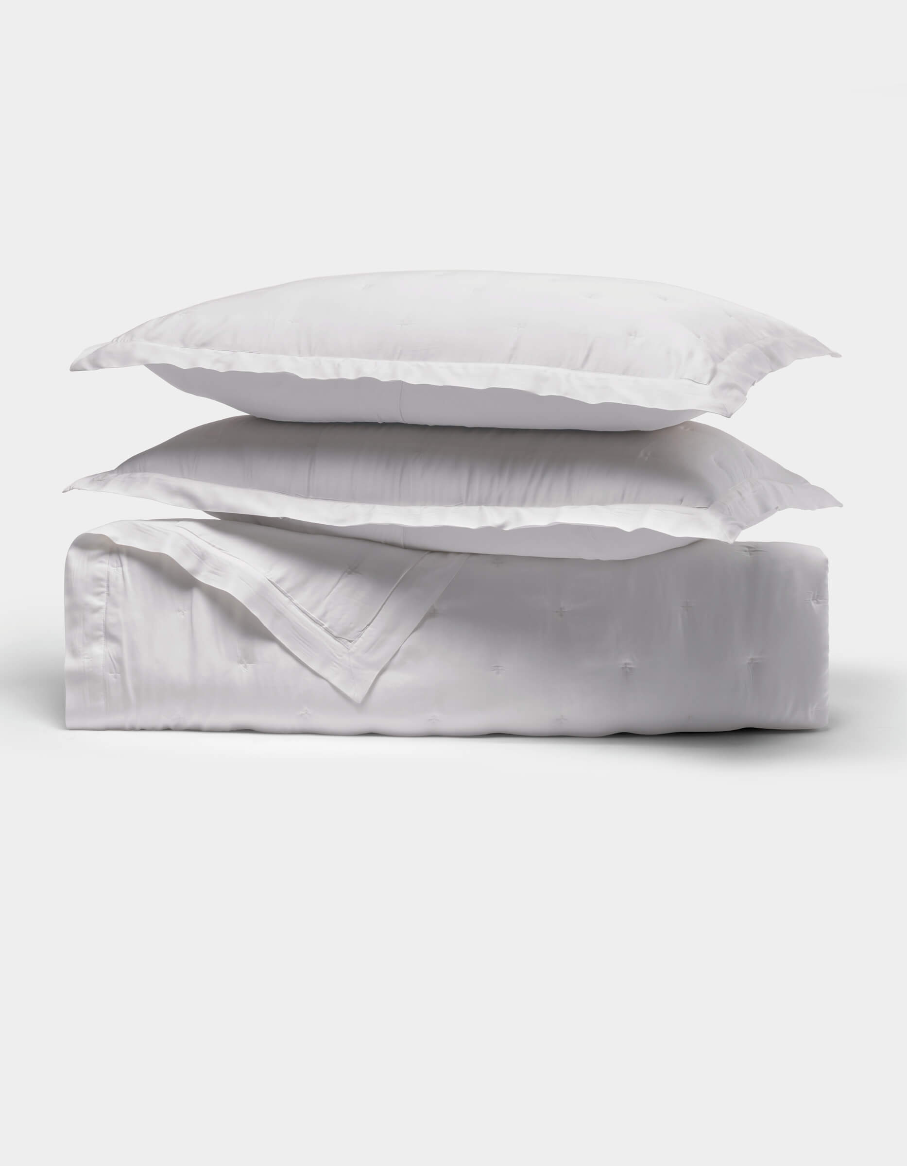 The Cozy Earth Bamboo Quilt Bundle features two fluffy white pillows stacked on a neatly folded white comforter, all shown against a plain white background.