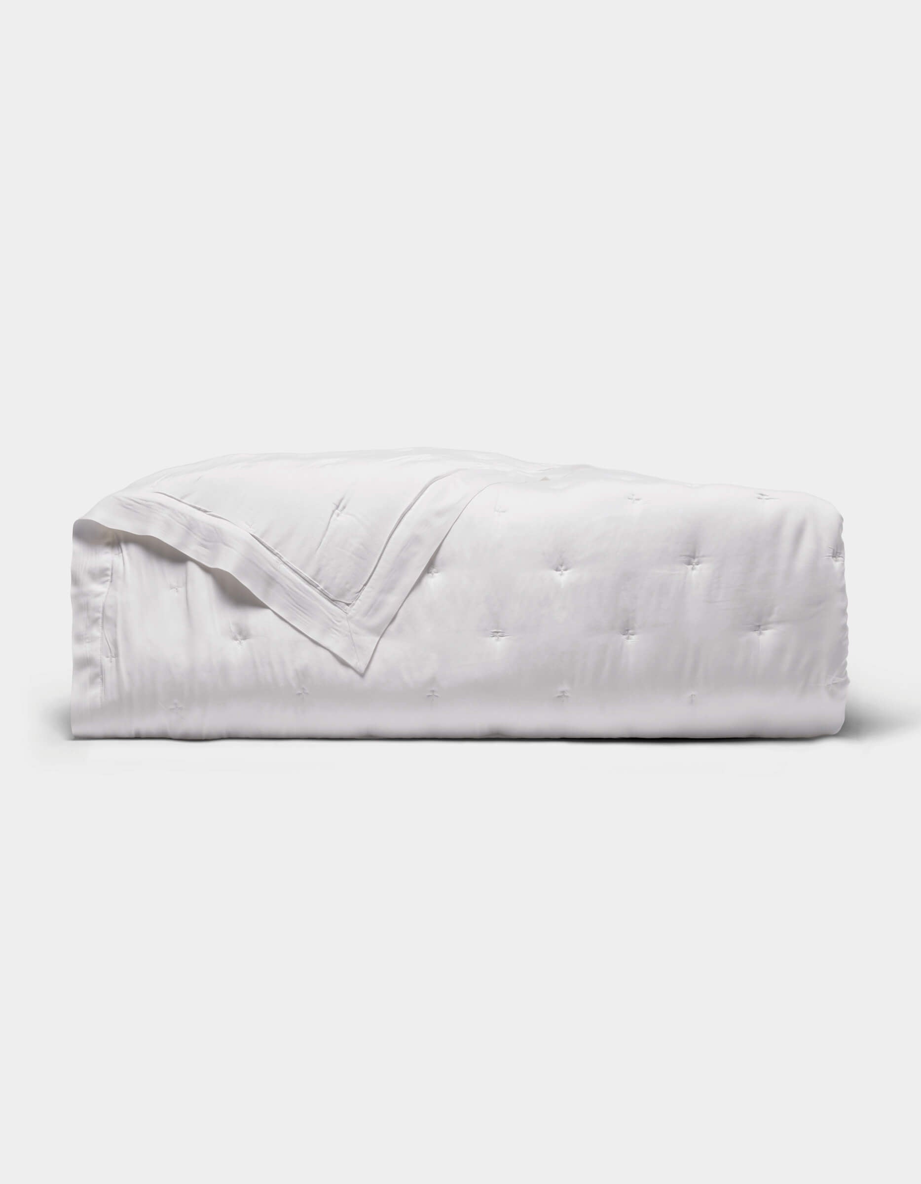 The Cozy Earth Bamboo Quilt is a neatly folded white quilt with a subtle quilted pattern, displayed against a plain light gray background.|Color:White