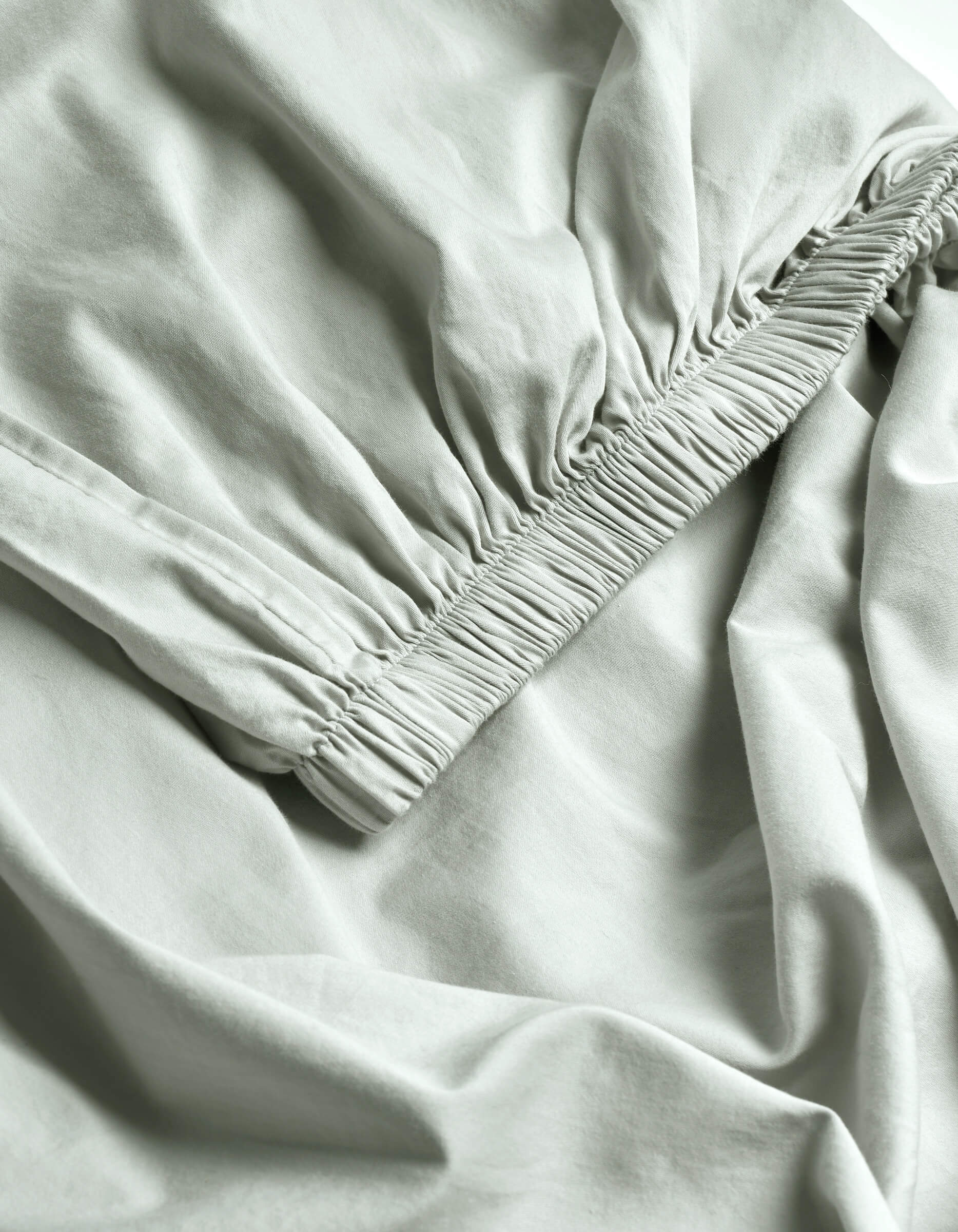 Close-up of Cozy Earth's Soft-Wash Cotton Fitted Sheet in light gray, featuring ruched elastic edges that create gentle folds and a textured, smooth, and lightweight surface.