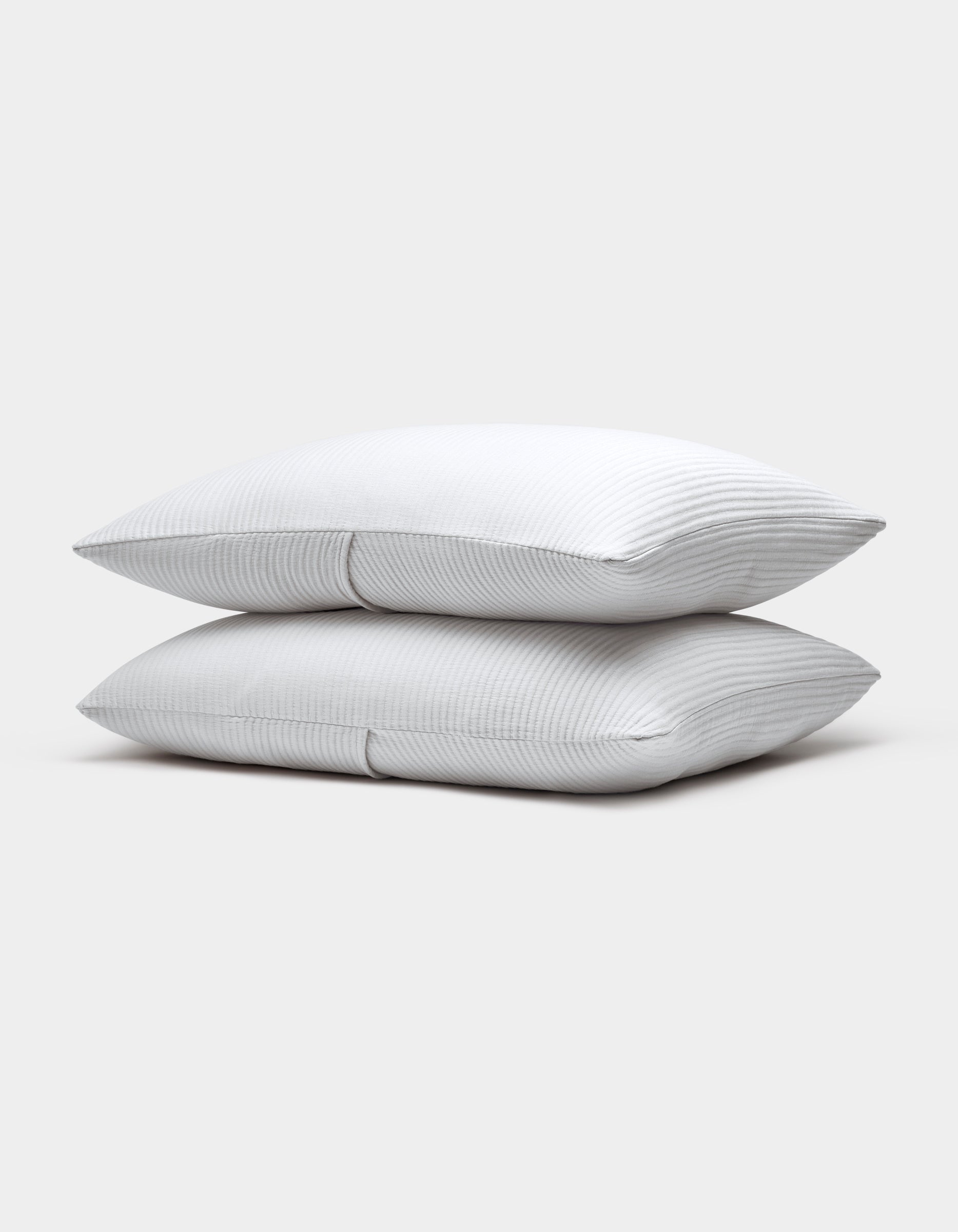 Two Cozy Earth Bamboo Coverlet Shams, white with subtle thin gray stripes, are stacked neatly atop each other against a plain light gray background.