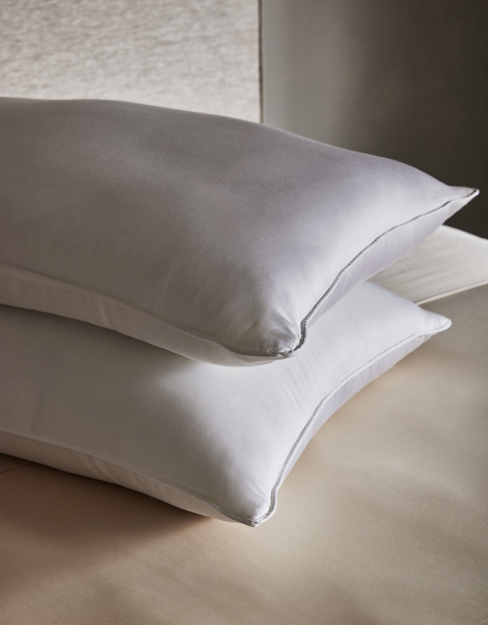 Two Cozy Earth Down Alternative Insert Bundle pillows are stacked on a light beige bed, set against a soft, neutral background for a calm and serene atmosphere.