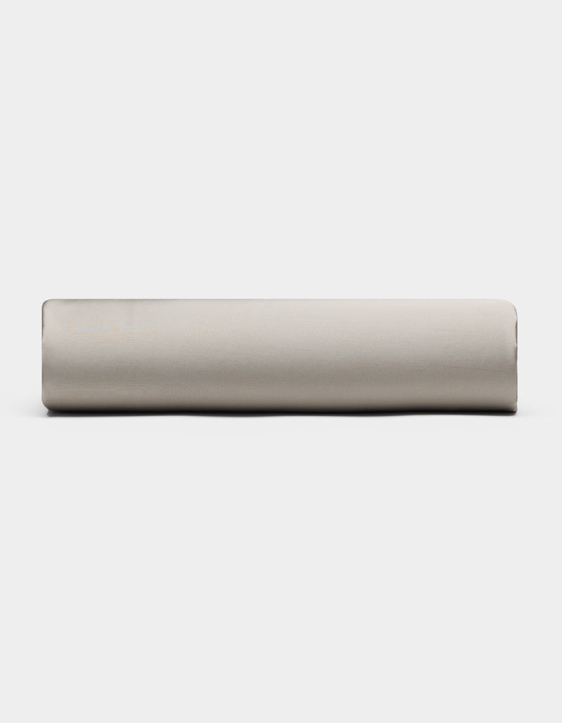 A Bamboo Fitted Sheet by Cozy Earth, in light gray, is rolled up and placed horizontally against a plain white background, viewed from the side.
