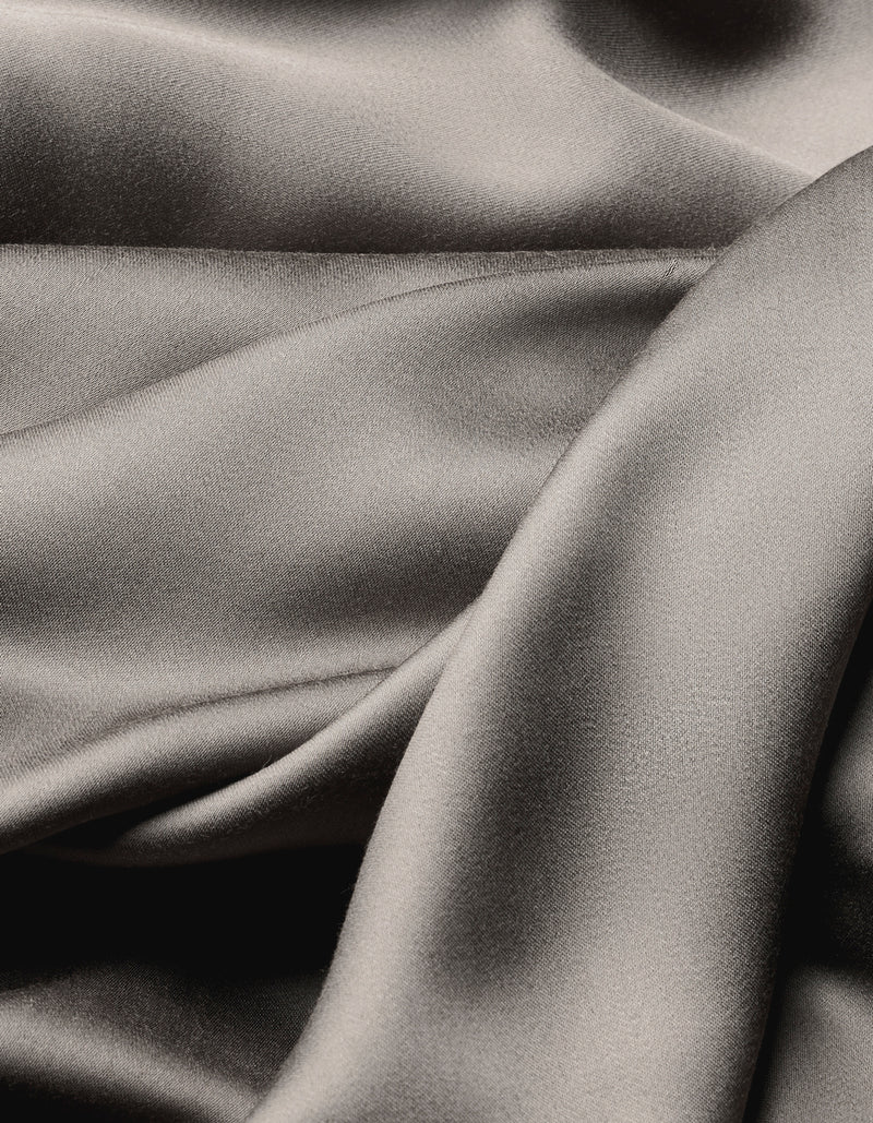 The Cozy Earth Bamboo Flat Sheet features smooth, folded silver-gray satin fabric with a soft sheen, offering an elegant, flowing texture and subtle highlights and shadows across the surface.