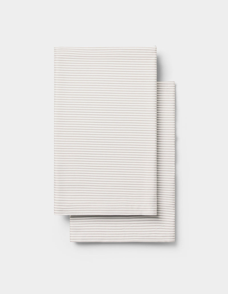 Two neatly folded, light-colored Cozy Earth Bamboo Pillowcases with thin, subtle horizontal stripes, placed one over the other on a plain white background.