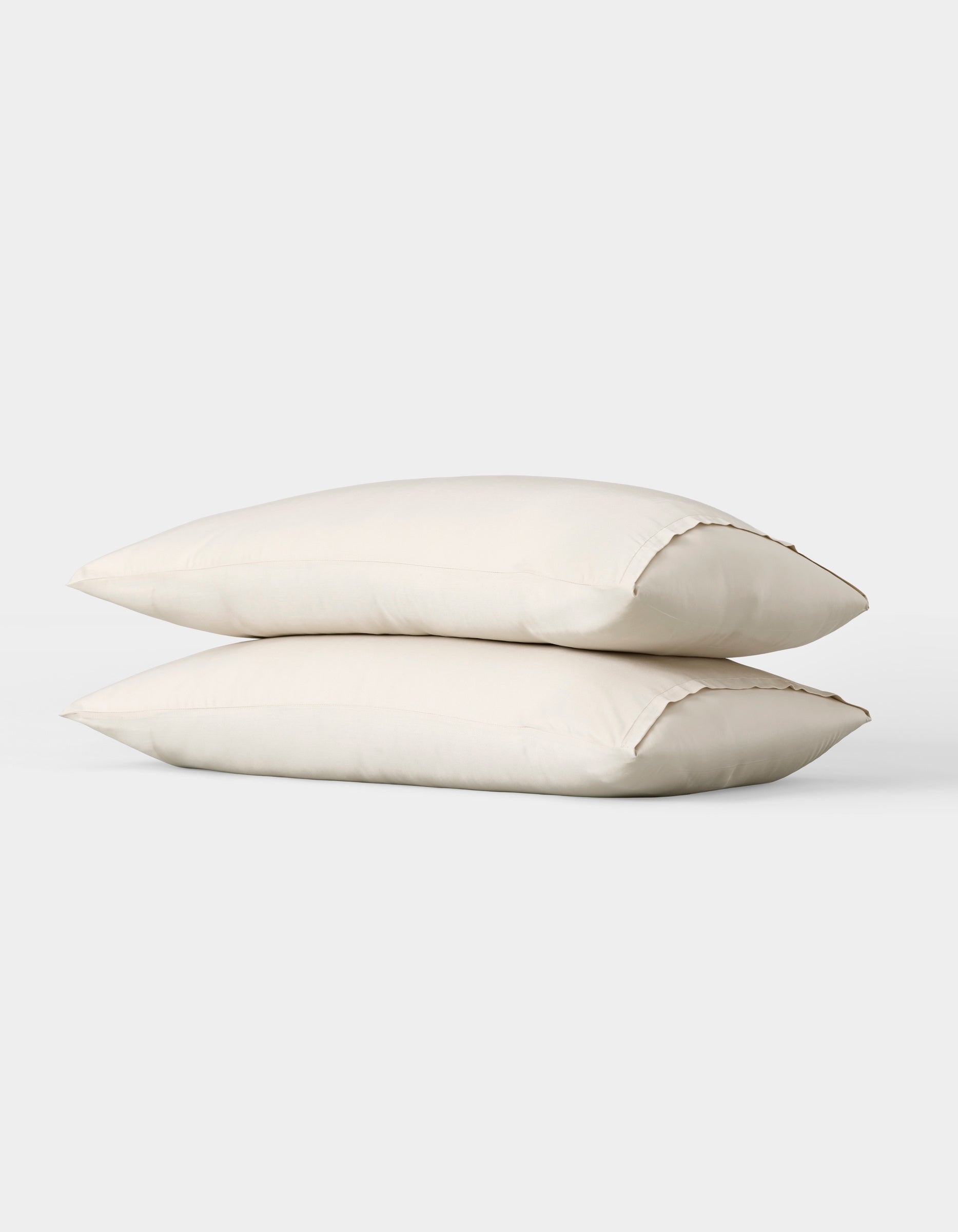 Two Bamboo Pillowcases by Cozy Earth, plain white, are stacked together against a simple light gray background. |Color:Oat