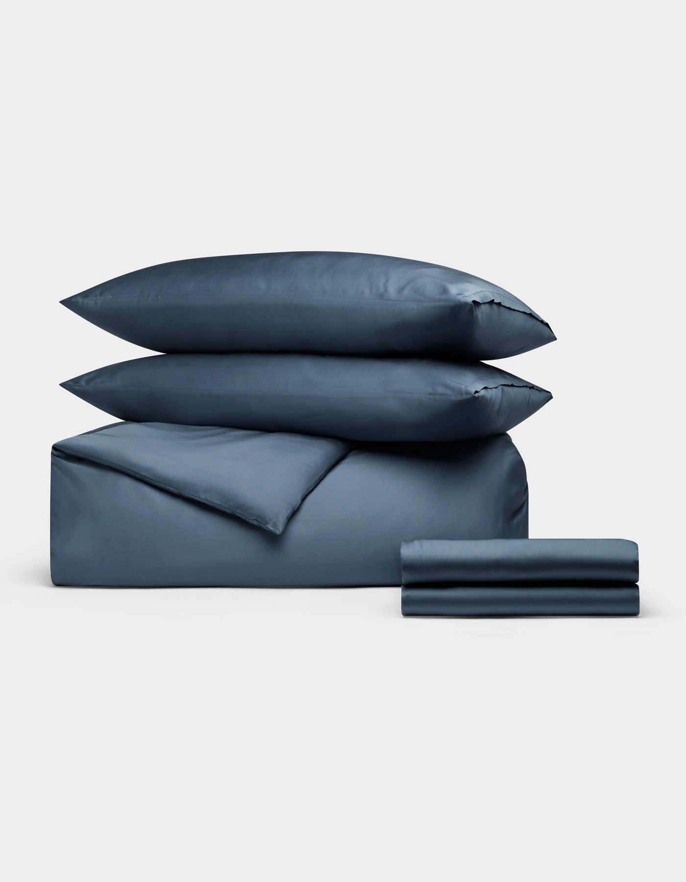 The Cozy Earth Bamboo Bedding Deluxe Bundle, featuring two pillows, a comforter, and folded sheets in blue, is neatly stacked against a plain light gray background.|Color:Pacific Blue