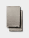 Two neatly folded Cozy Earth Silk Pillowcases in light gray are stacked together against a plain white background.|Color:Charcoal