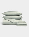 A neatly stacked Cozy Earth Bamboo Bedding Ultimate Bundle, featuring two pillows, a folded duvet, and folded sheets in pale green, displayed against a plain white background.|Color:Laurel