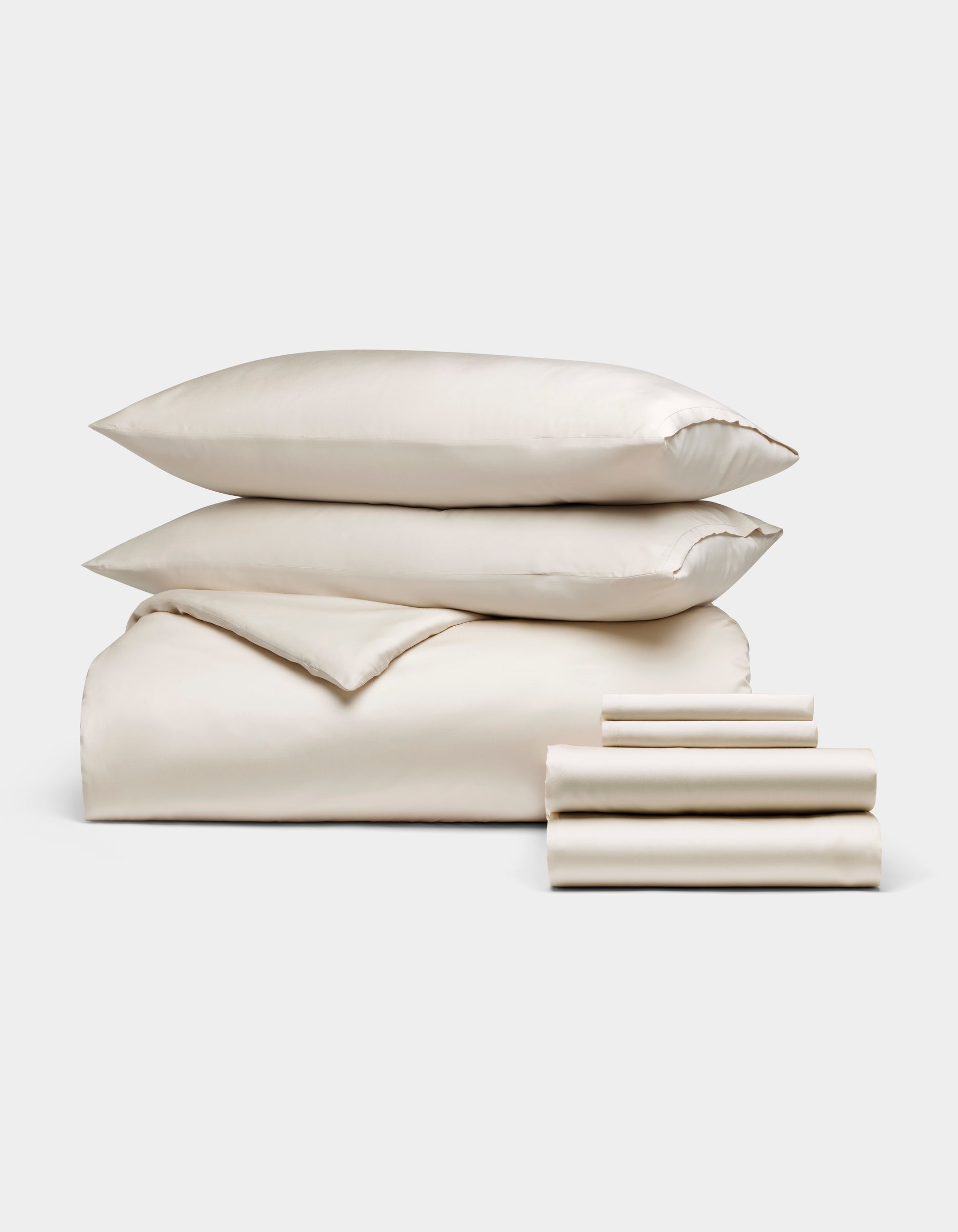 The Cozy Earth Bamboo Bedding Ultimate Bundle, featuring ivory-colored bed linens with two pillows, a folded comforter, and stacked sheets, is displayed against a plain white background.|Color:Oat