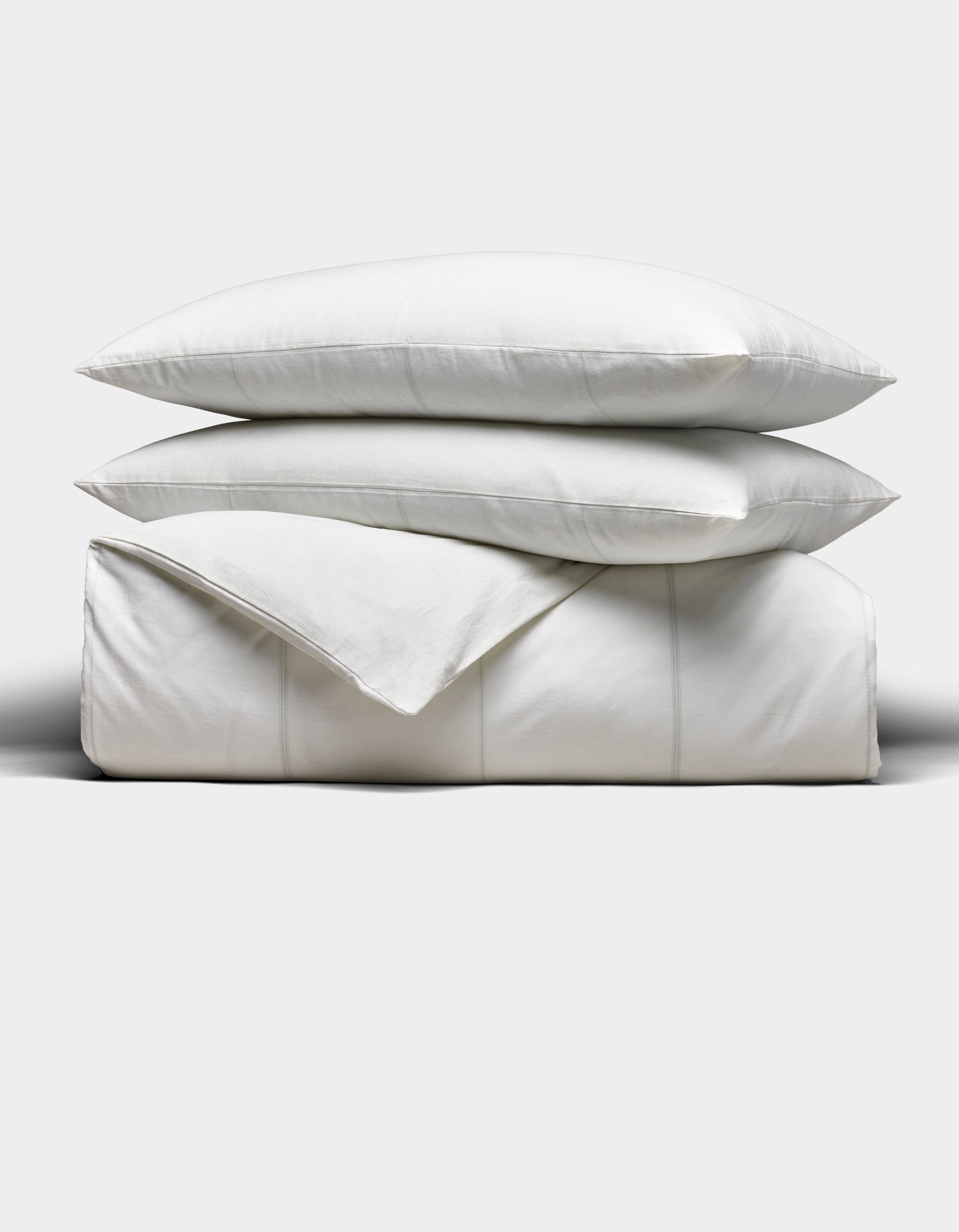 The Cozy Earth Baja Duvet Bundle features two white pillows stacked on a neatly folded white duvet, all set against a plain light grey background.|Color:Laurel Stripe/Striped Bone