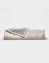 The Cozy Earth Baja Matelasse Coverlet features a neatly folded design with a cream side adorned with subtle lines and a textured gray reverse, shown against a plain white background.|Color:Alabaster/Oceanside
