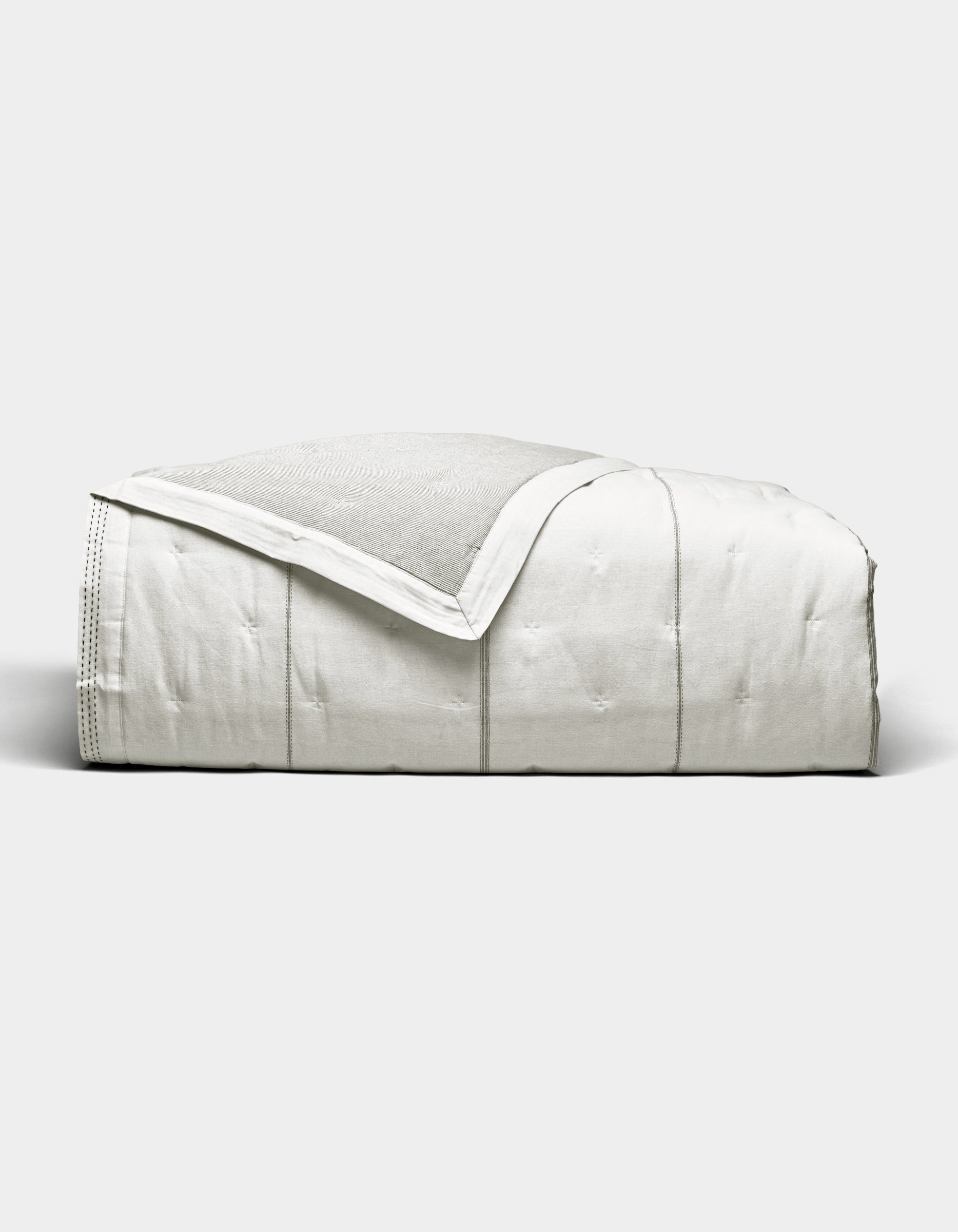 The Cozy Earth Baja Quilt, featuring stitched detailing, is neatly folded and displayed against a plain light gray background.|Color:Laurel Stripe/Striped Bone