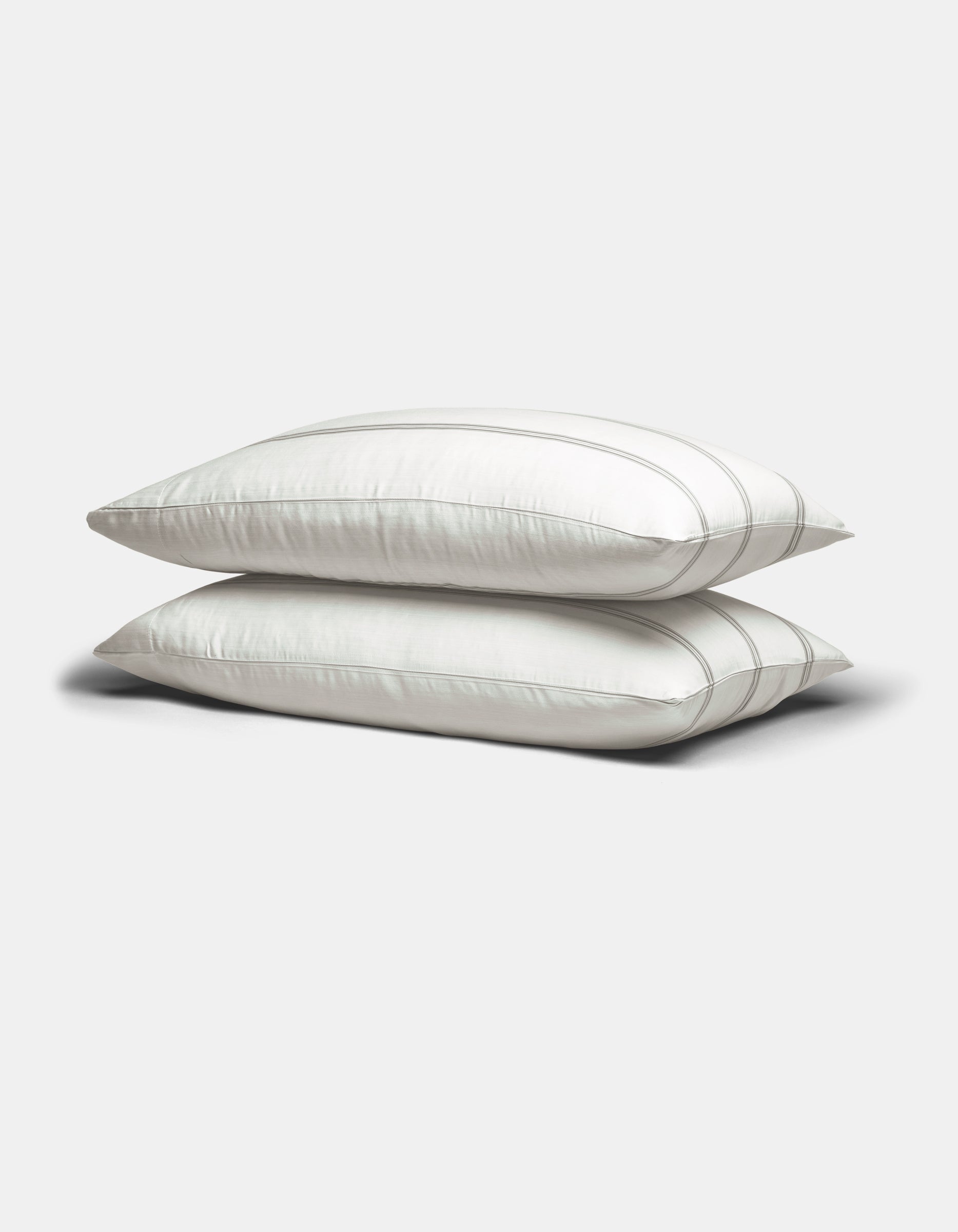 Two Cozy Earth Bamboo Pillowcases in white with subtle gray stripes are stacked on a plain light gray background.|Color:Baja Stripe in Laurel