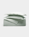The Cozy Earth Linen Duvet Set in sage green features a neatly folded duvet and two stacked pillowcases, all showcased against a plain white background.|Color:Mist