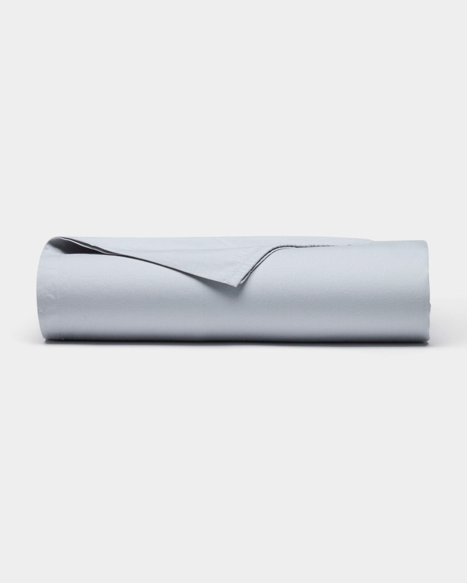 The Soft-Wash Cotton Sheet Set by Cozy Earth is shown neatly rolled up in light gray on a plain white background, with one corner gently lifted.