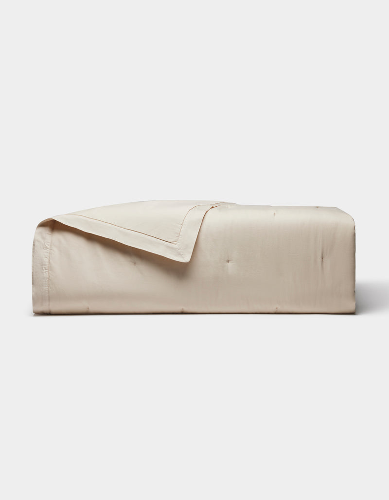 The Cozy Earth Soft-Wash Cotton Quilt, featuring a smooth quilted design in light beige, is neatly folded against a plain white background.