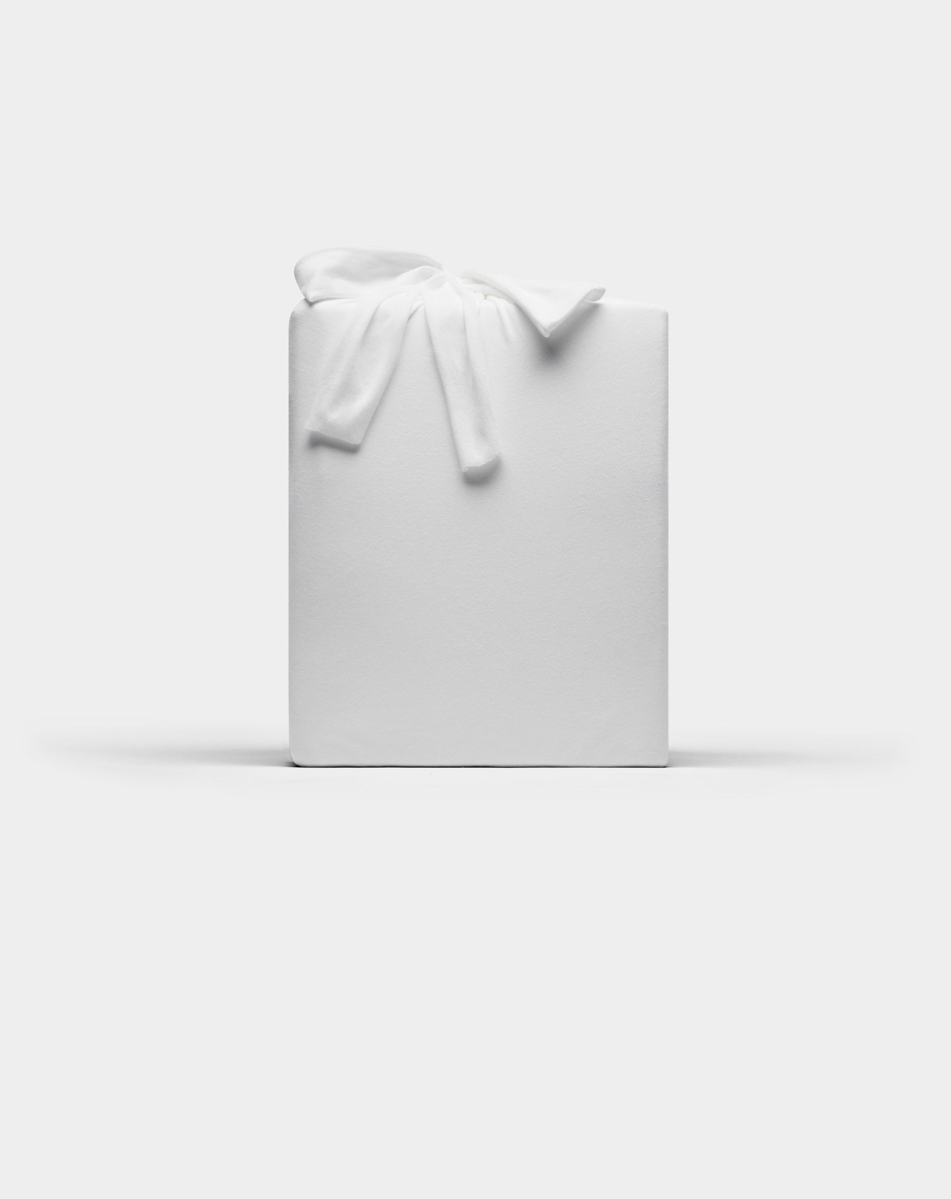 A Bamboo Jersey Sheet Set by Cozy Earth, wrapped in plain white paper with a white fabric bow on top, set against a plain white background.