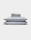 The Cozy Earth Bamboo Jersey Sheet Set is shown neatly stacked with two pillows at the bottom and folded light gray sheets and pillowcases on top, all set against a plain white background.|Color:Shore