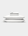 Two white Cozy Earth Bamboo Jersey Sheet Set sheets are neatly folded atop two stacked pillows, all set against a plain white background.|Color:White