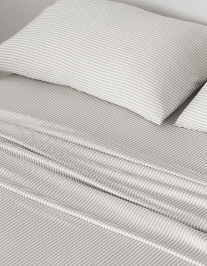 A neatly made bed showcases Cozy Earth Bamboo Pillowcases and sheets with thin, light gray and white horizontal stripes, giving the bedding a smooth, clean look that creates a calm and cozy atmosphere.