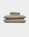 The Cozy Earth Bamboo Sheet Set, featuring striped beige and black sheets and pillowcases, is neatly stacked on two large pillows against a plain white background.|Color:Classic Stripe in Ebony