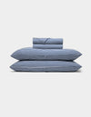 A neatly folded Bamboo Sheet Set by Cozy Earth, featuring blue and white stripes, with two pillows, a duvet, and a folded sheet stacked against a plain white background.|Color:Classic Stripe in Pacific