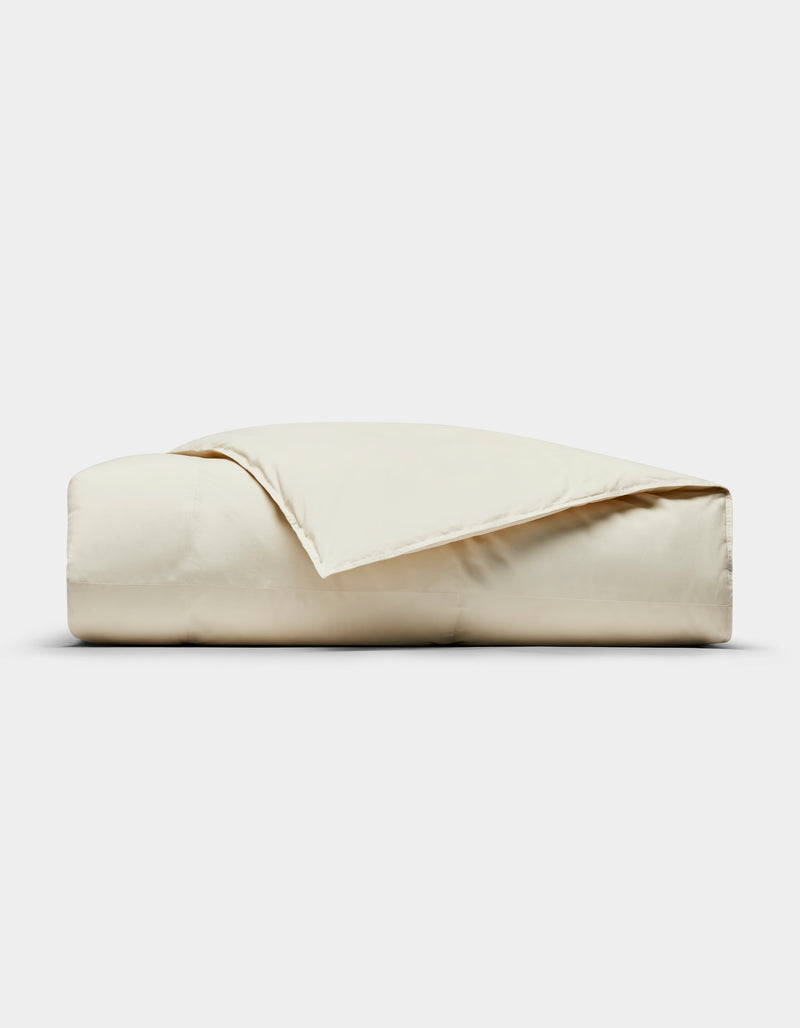 The Cozy Earth Down Alternative Throw, neatly folded in light beige with one corner slightly flipped open, is displayed against a plain white background.