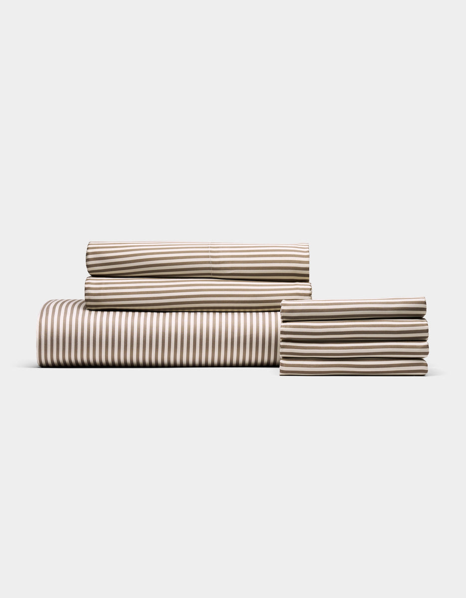 The Cozy Earth Bamboo Bedding Core Bundle features a neatly folded set of tan and white striped sheets—including a fitted sheet, flat sheet, and pillowcases—displayed against a plain white background.|Color:Classic Stripe in Ebony