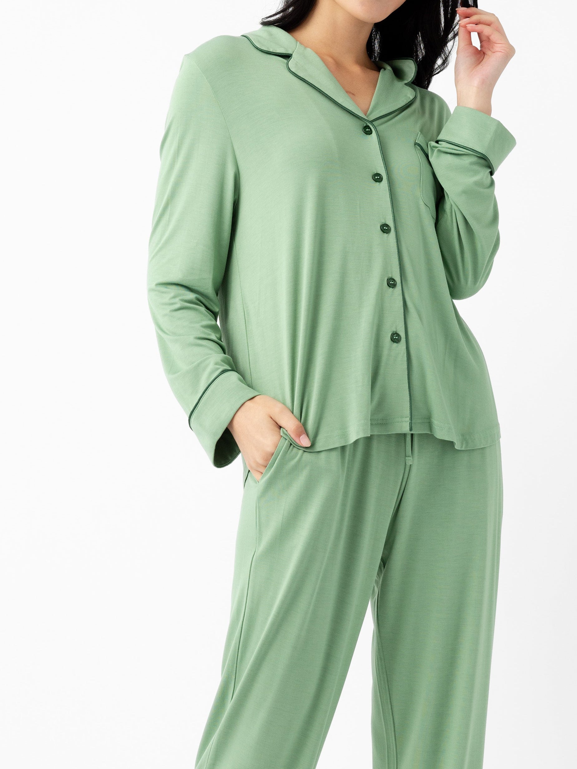 A woman wears the Cozy Earth Last Chance Women's Bamboo Stretch-Knit Long Sleeve Pajama Set in light green, featuring a loose fit, button-up top, and matching pants, with one hand in her pocket against a plain white background.|Color:Fern