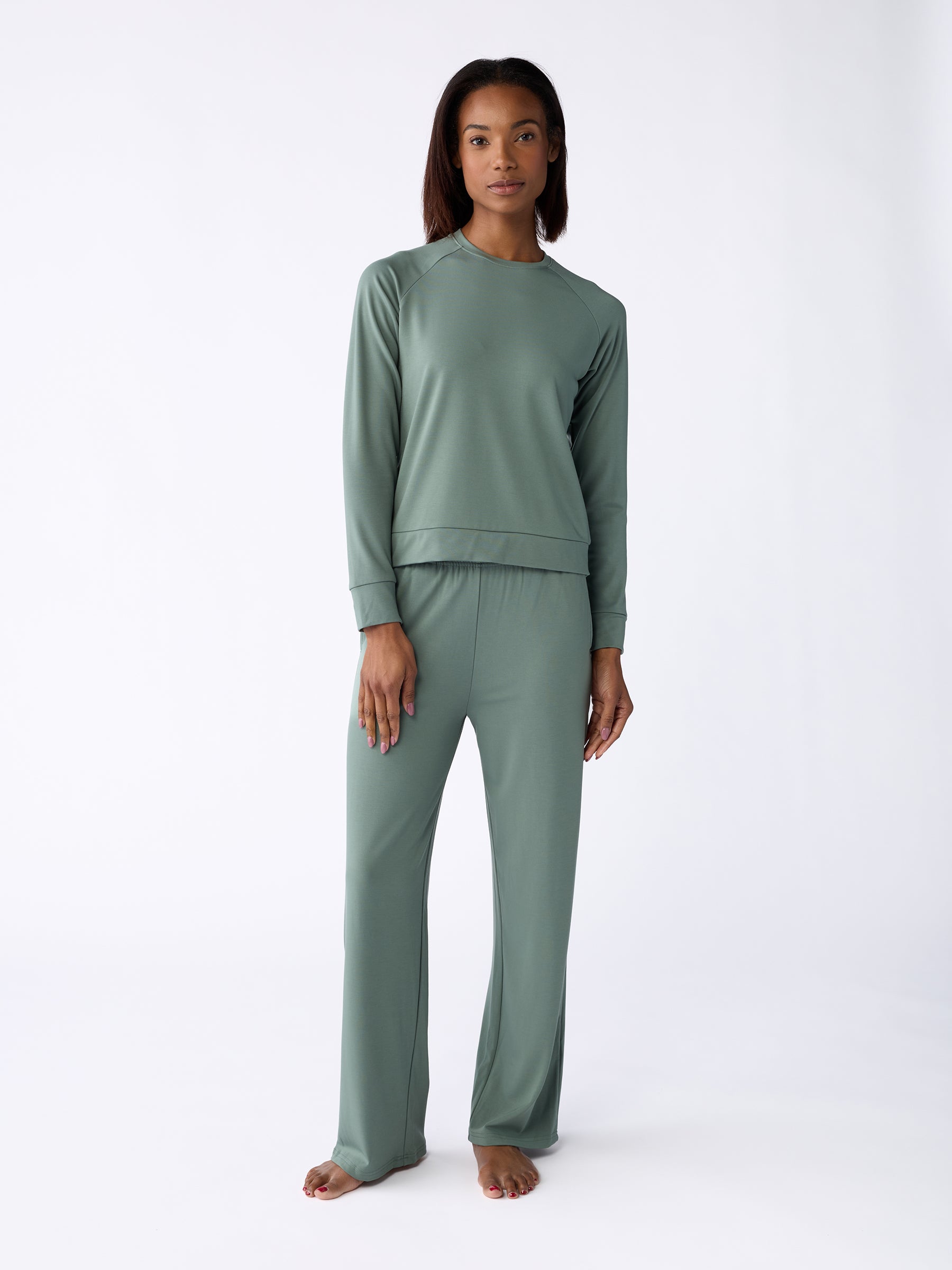 A person dressed in a comfortable green ensemble from Cozy Earth stands barefoot against a plain white background, featuring the Women's Ultra-Soft Bamboo Wide Leg Pull On Pant TALL paired with a long-sleeve top. |Color:Oakmoss