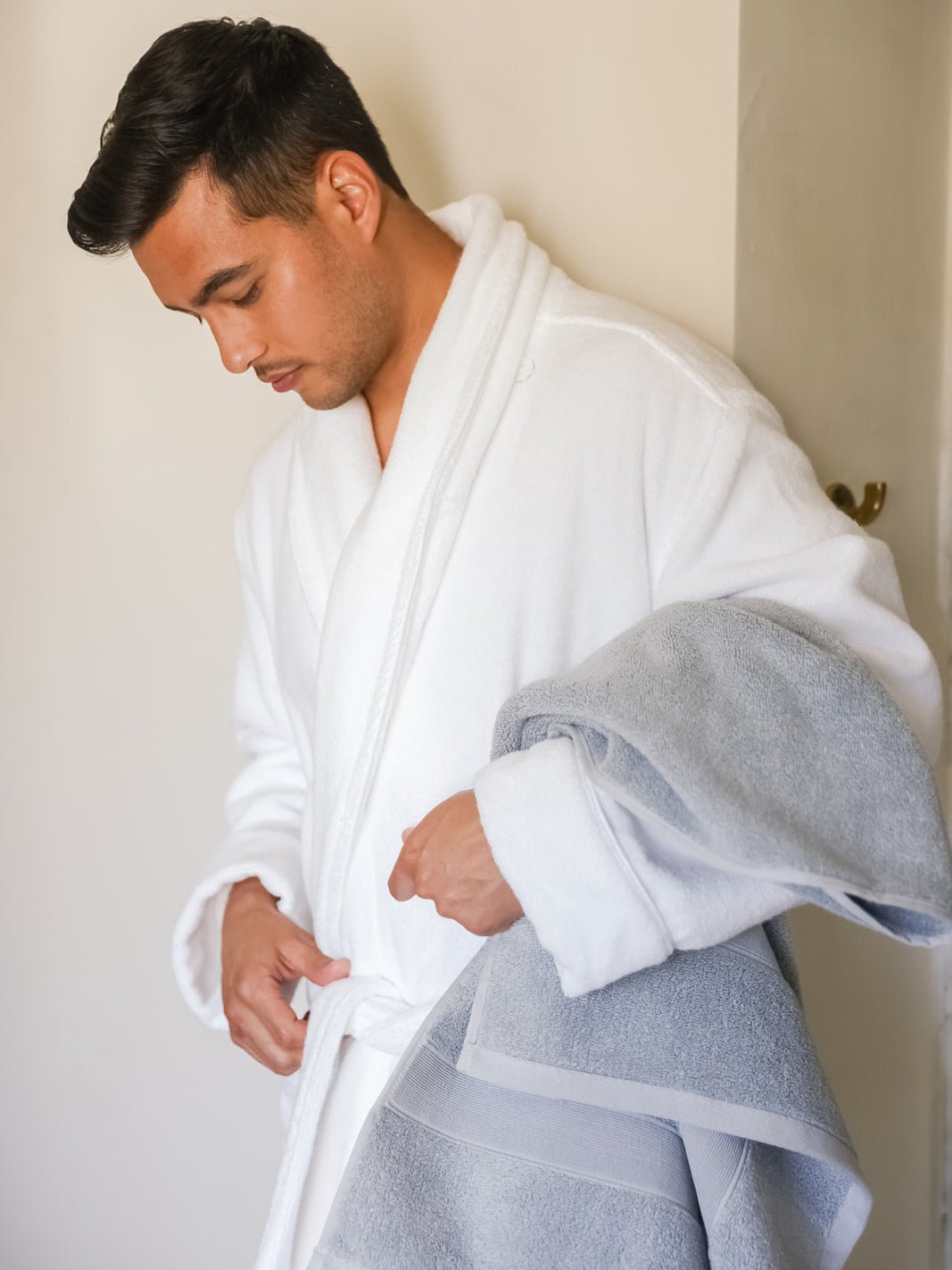 Man wearing white robe holding harbor mist luxe bath sheet 