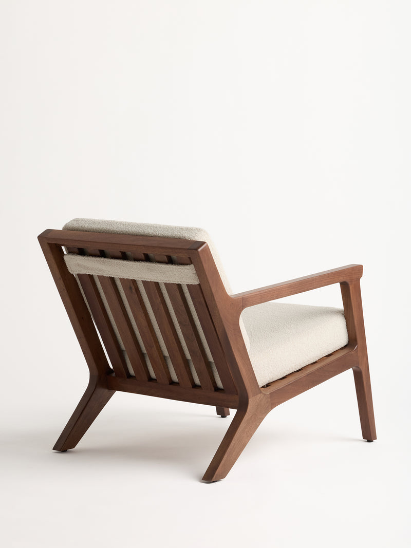 Introducing the Coronado Lounge Chair by Cozy Earth, featuring a sleek wooden frame complemented by a beige cushioned seat and backrest. The chair is angled to the right, highlighting its clean lines and minimalist design against a plain white background.