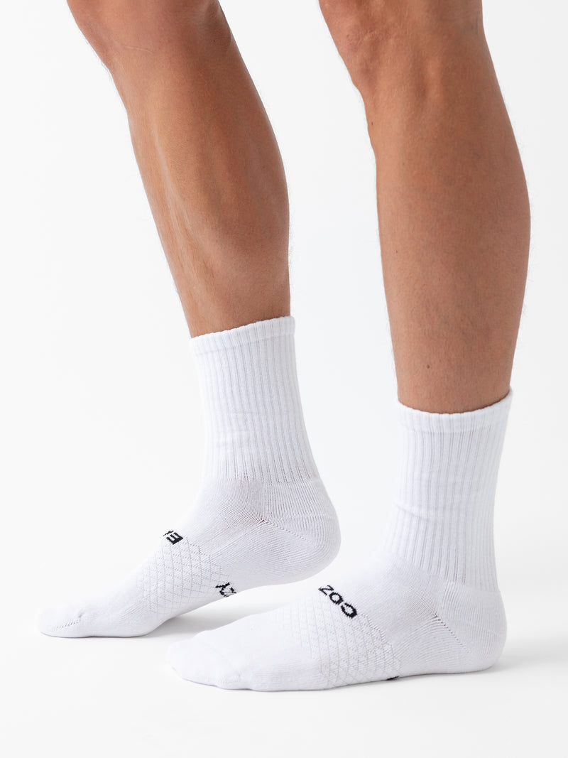 A person wears Cozy Earth Essential Calf Socks from the 8-Pack, featuring a ribbed texture and white color, with "BOSS" visible near the toes, standing on a white background.