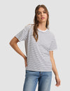 A woman models the Cozy Earth Women's All Day Tee—a white t-shirt with black stripes—paired with blue jeans, standing against a light gray background and looking at the camera, one hand on her hip. |Color:Jet Black Stripe