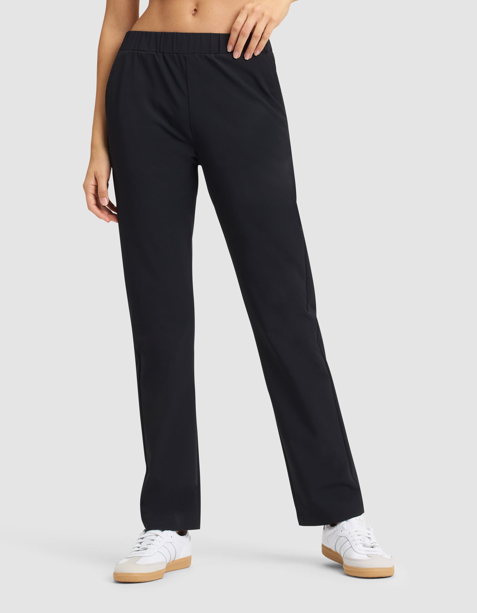 A woman models the Cozy Earth Women's Always Pant in black with white sneakers, standing against a plain light gray background; only her lower torso and legs are shown. 
