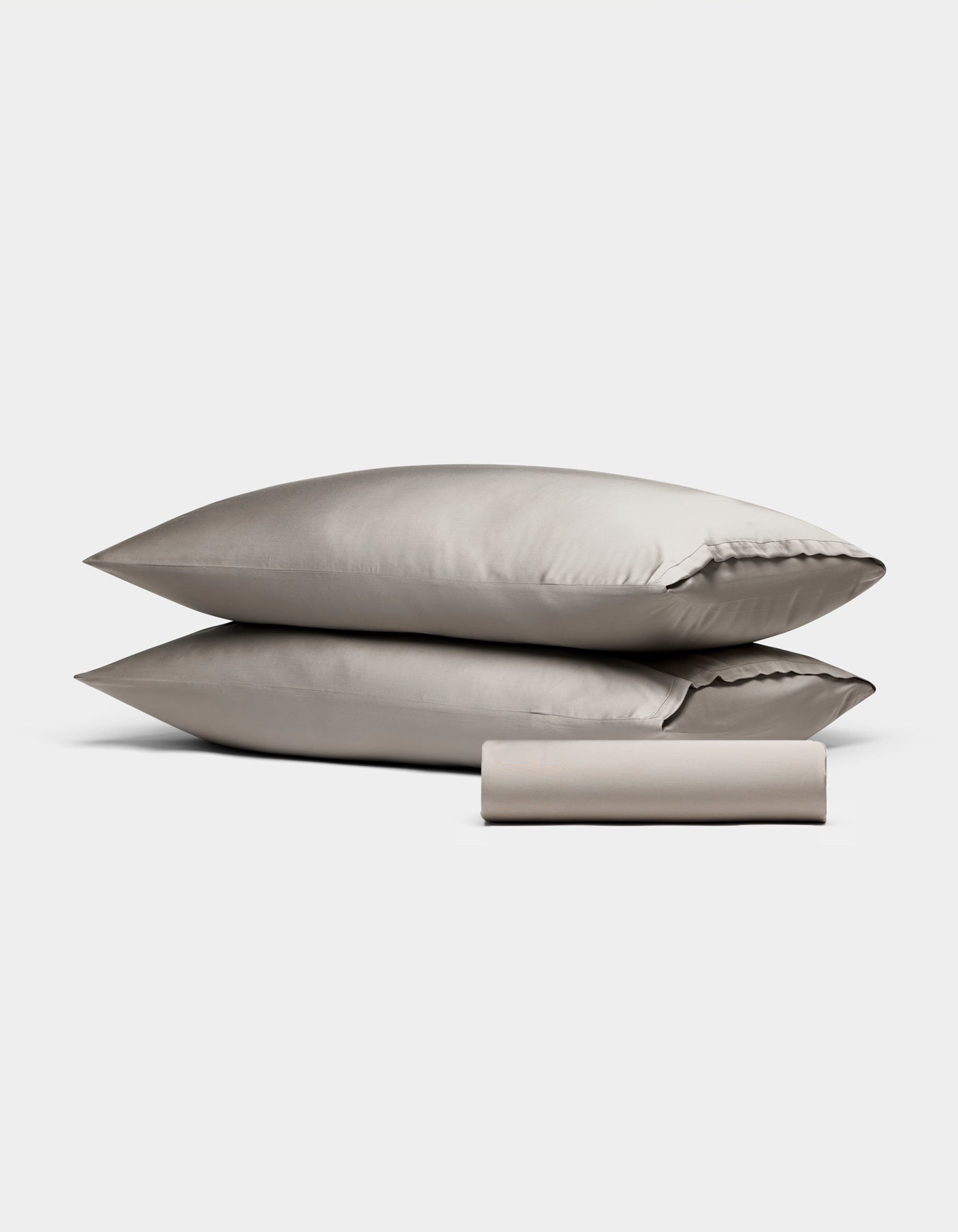 The Cozy Earth Bamboo Bedding Basic Bundle features two stacked beige pillows and a neatly rolled matching beige sheet, all set against a plain white background.