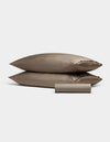 Two taupe Bamboo Bedding Basic Bundle pillowcases by Cozy Earth are stacked together, with a matching cylindrical fabric pouch in front, all set against a plain light gray background.|Color:Walnut