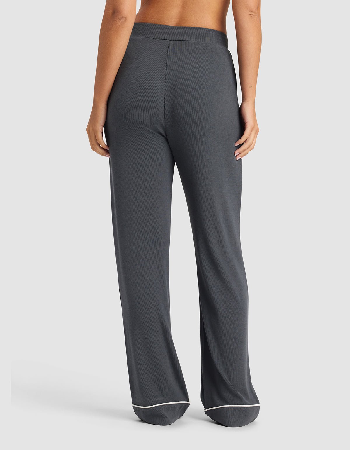 A woman is shown from the back wearing Cozy Earth's Women's Bamboo Rib-Knit Classic Pajama Pant in dark gray with white trim, standing barefoot against a plain light background.