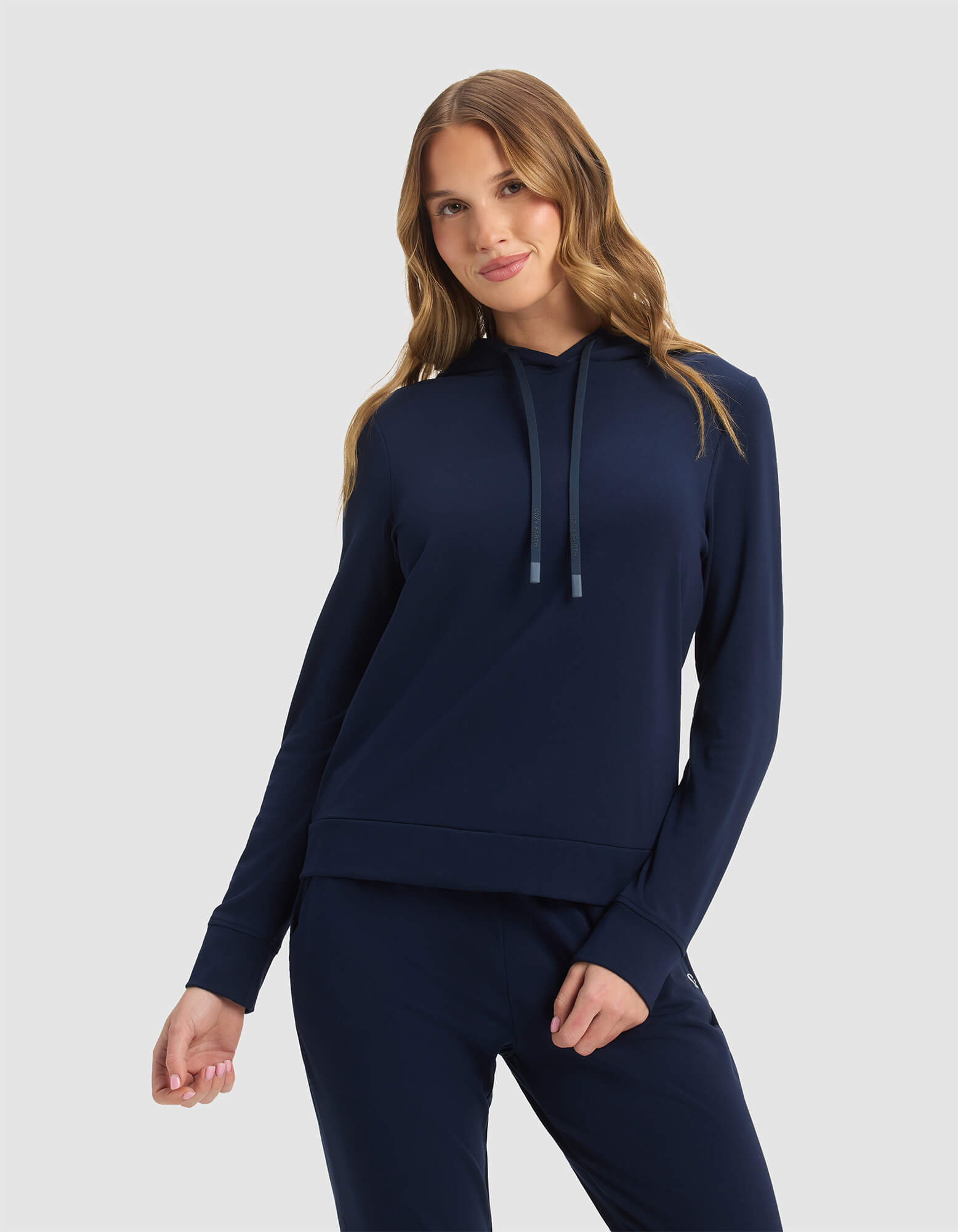 A woman with long, wavy light brown hair smiles gently, wearing the Cozy Earth Women's Brushed Bamboo Hoodie in navy against a plain light gray background.|Color:Navy