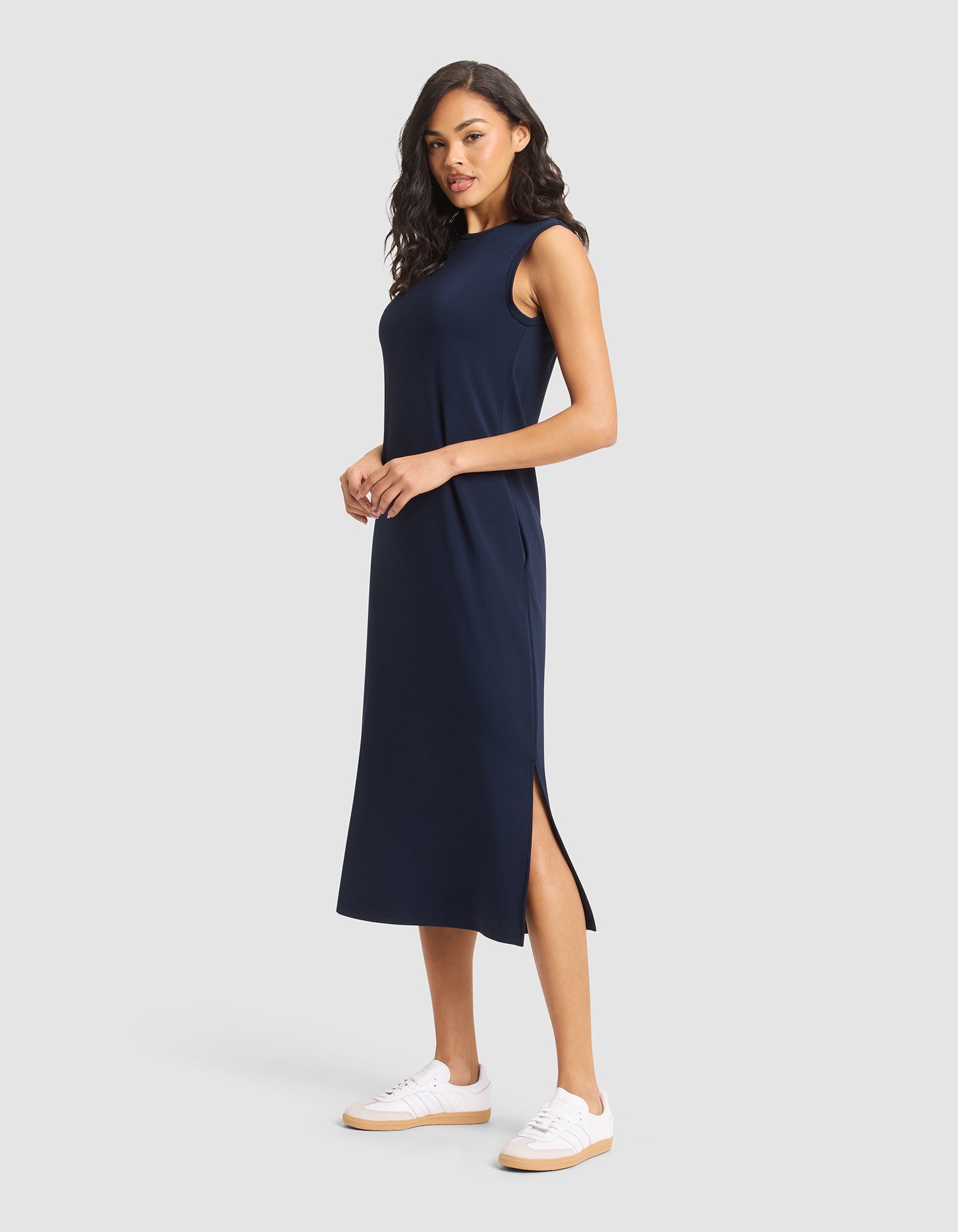 A woman in a Cozy Earth Women's Brushed Bamboo Sleeveless Midi Dress and white sneakers stands against a plain light gray background. |Color:Navy